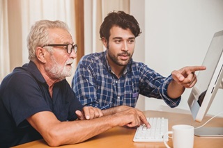 Picture of someone helping at senior at a PC.